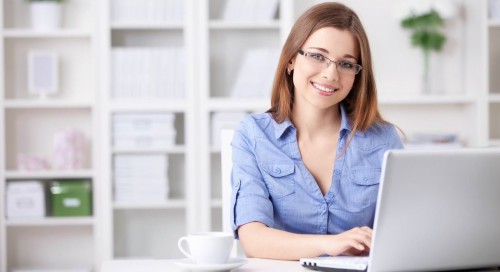 Красивая девушка в очках сидит за столом за ноутбуком